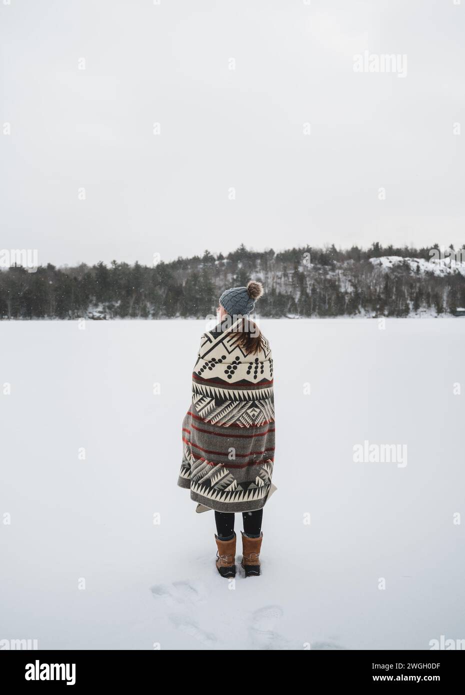 Femme enveloppée dans une couverture sur la rive du lac gelé le jour d'hiver. Banque D'Images