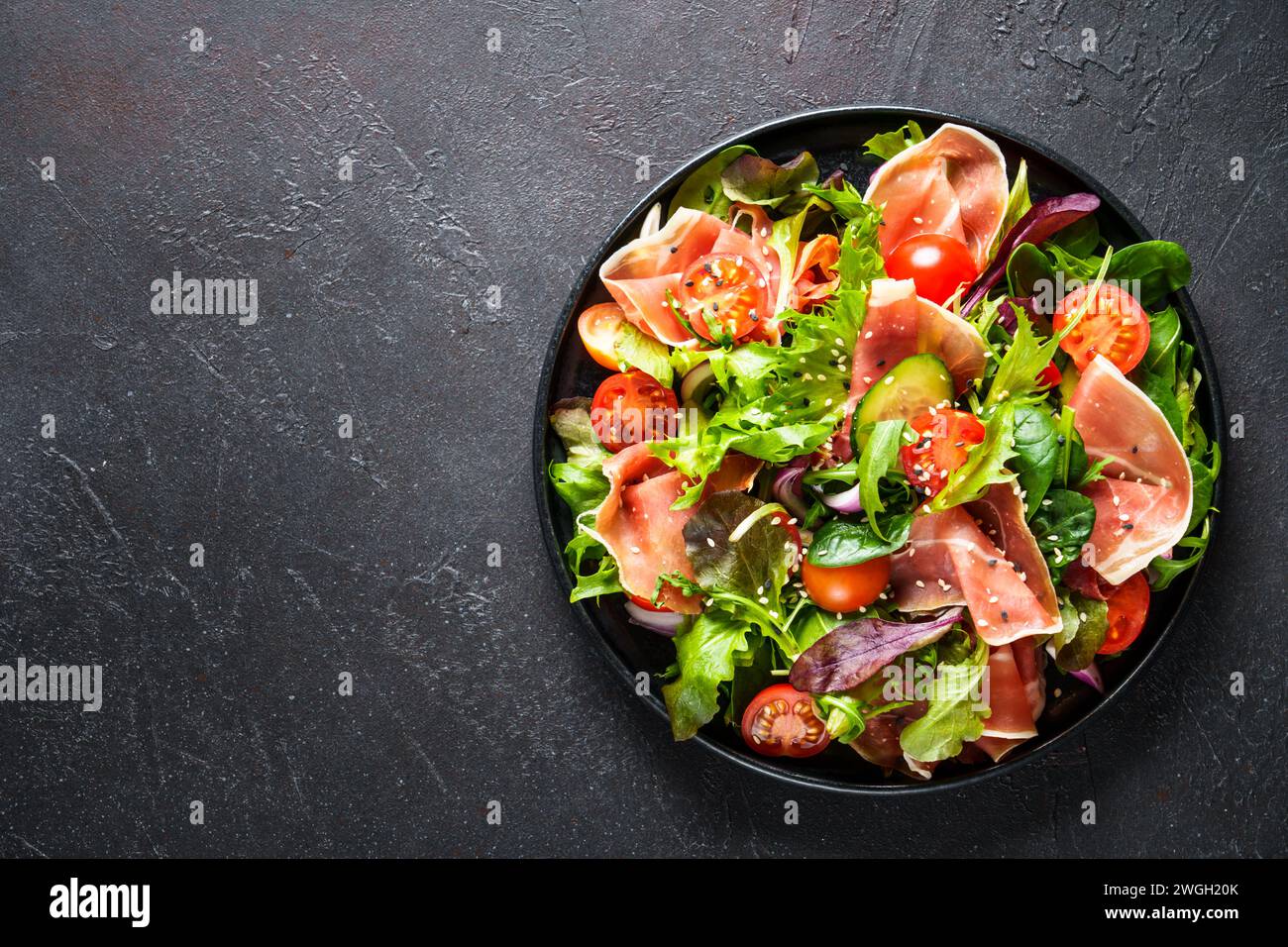 Salade verte sur fond noir. Feuilles de salade vertes, viande fumée et tomates. Vue de dessus avec espace pour le texte. Banque D'Images