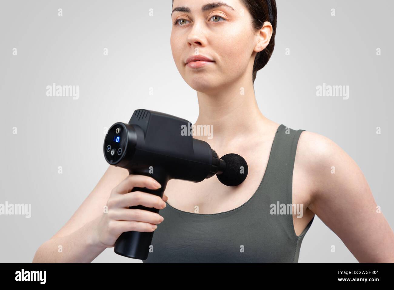 Portrait de jeune femme caucasienne se donne massage sur la poitrine avec masseur-pistolet à percussion avec buse à bille. Fond gris. Traitement de l'IAP articulaire Banque D'Images