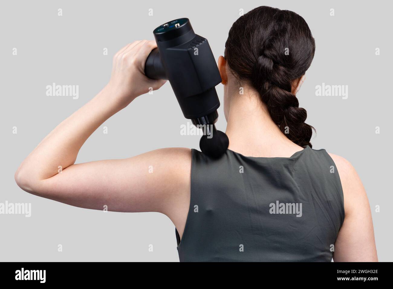 Vue arrière de la femme en forme se donne elle-même massage sur le haut du bras avec masseur-pistolet à percussion. Fond de studio gris. Traitement pour soulager les douleurs articulaires. Banque D'Images