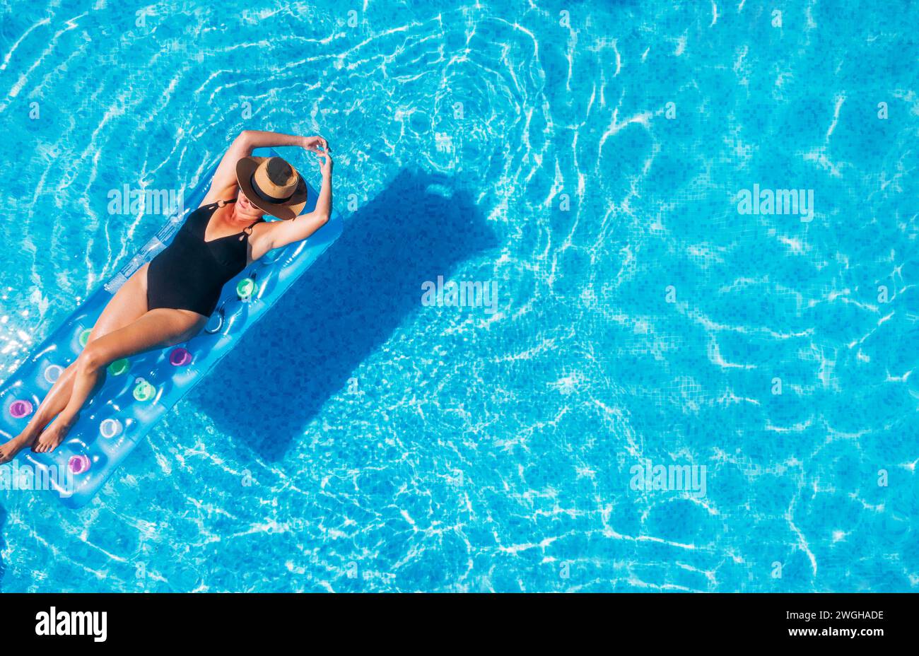 Sexy jeune femme en maillot de bain noir, dans un chapeau de paille et des lunettes de soleil flottant sur les vagues bleues de la piscine sur le matelas gonflable. Détendez-vous Banque D'Images