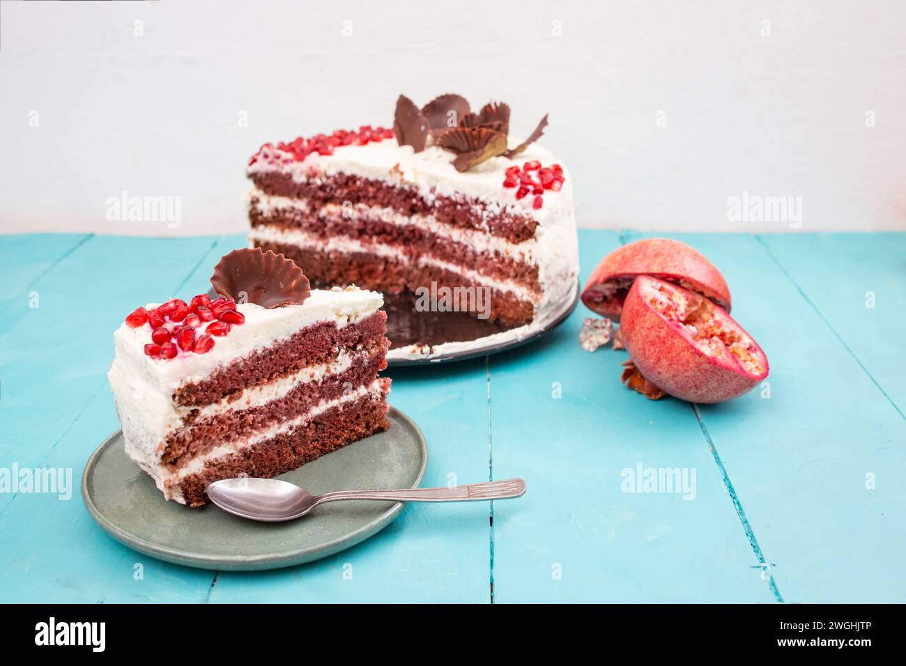 Gâteau de velours rouge aux graines de grenade, tranché sur une plaque en céramique, sur une table de planches en bois bleu Banque D'Images