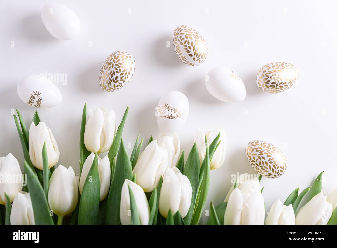 Bordure florale de bouquet de tulipes blanches, oeufs de Pâques et jouets sur fond blanc. Concept de célébration de Pâques. Espace de copie. Vue de dessus Banque D'Images