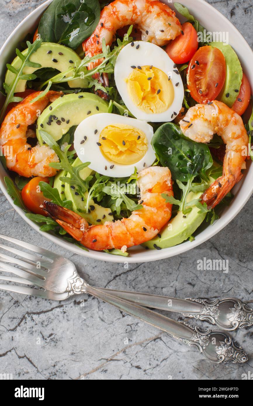 Salade biologique diététique saine avec crevettes, avocat, roquette, épinards, tomates, graines de sésame et œufs durs gros plan dans un bol sur la table. Vertical Banque D'Images