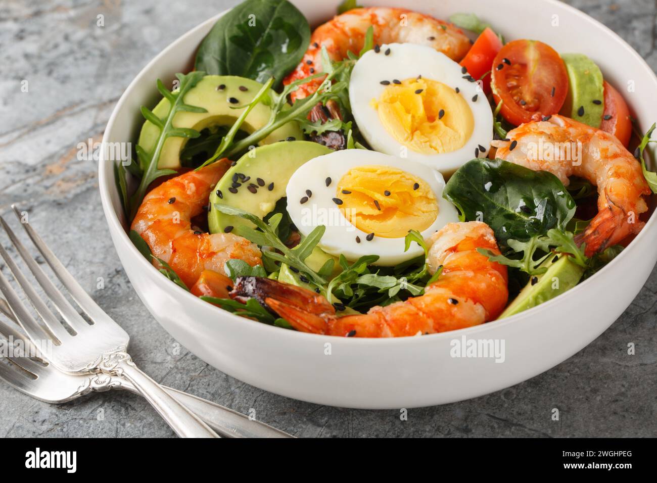 Salade de petit déjeuner équilibrée avec crevettes, avocat, roquette, épinards, tomates et œufs durs gros plan sur un bol sur la table. Horizontal Banque D'Images