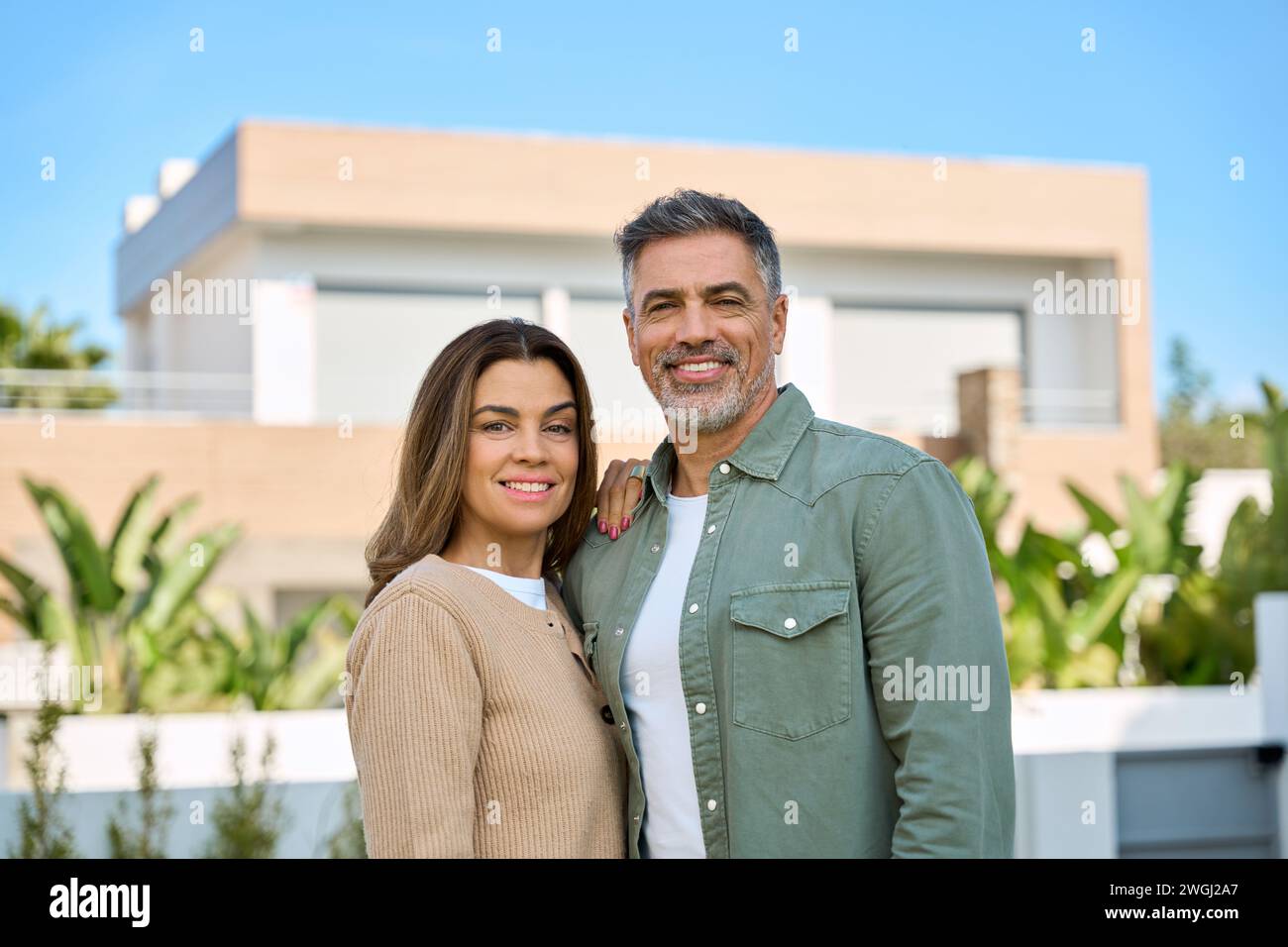 Heureux souriant couple d'âge moyen acheteurs de nouvelles propriétés debout à l'extérieur de la maison. Banque D'Images