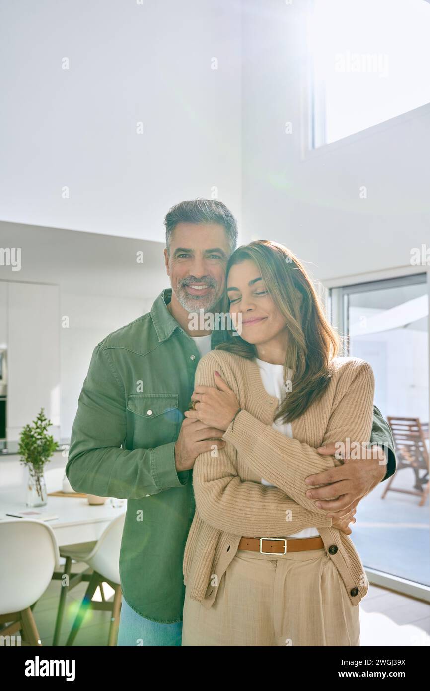 Heureux couple d'âge moyen serrant regardant la caméra debout à la maison. Vertical. Banque D'Images