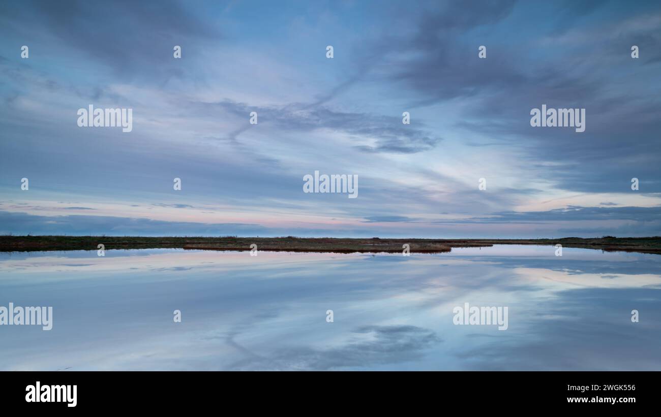 Vaste tranquillité dans la réserve naturelle de Vatrop au bord de la mer des Wadden. Les nuages doux sont légèrement colorés par le soleil couchant et se reflètent dans l'eau calme. Banque D'Images