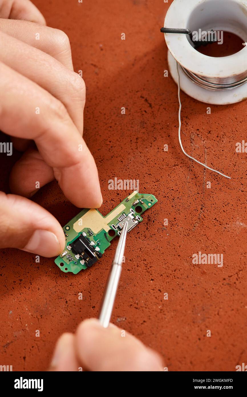 vue rognée d'un réparateur professionnel avec une pince à épiler testant le chipset électronique en atelier Banque D'Images