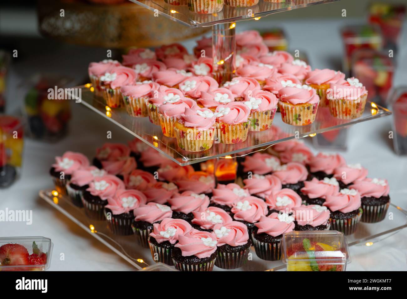 Cupcakes d'anniversaire sur le présentoir en verre à trois niveaux festif fleur blanche rose gros plan Banque D'Images