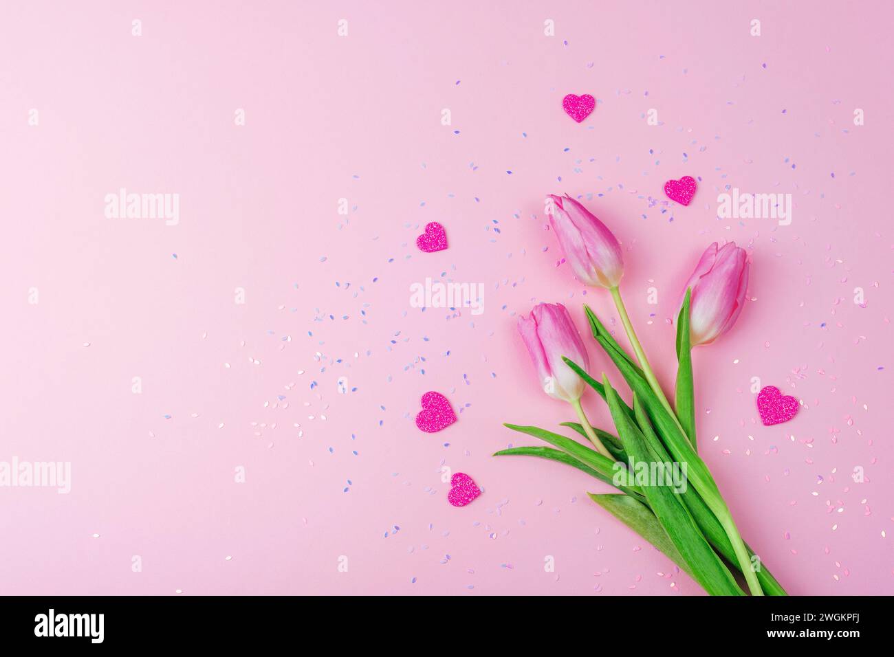 Tulipes roses et coeurs sur fond avec des confettis. Saint-Valentin, concept de la journée des femmes. Vue de dessus, pose à plat, espace de copie. Banque D'Images