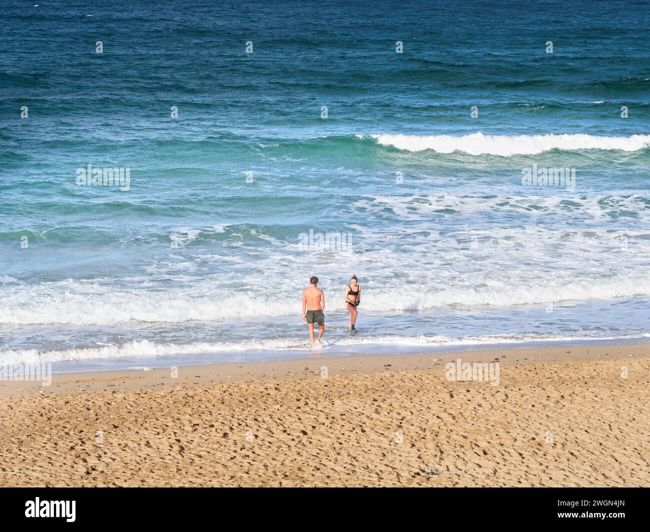 Un couple de nageurs dans l'océan Atlantique à Fistral Beach, Cornwall, Angleterre, par une journée ensoleillée d'hiver. Banque D'Images