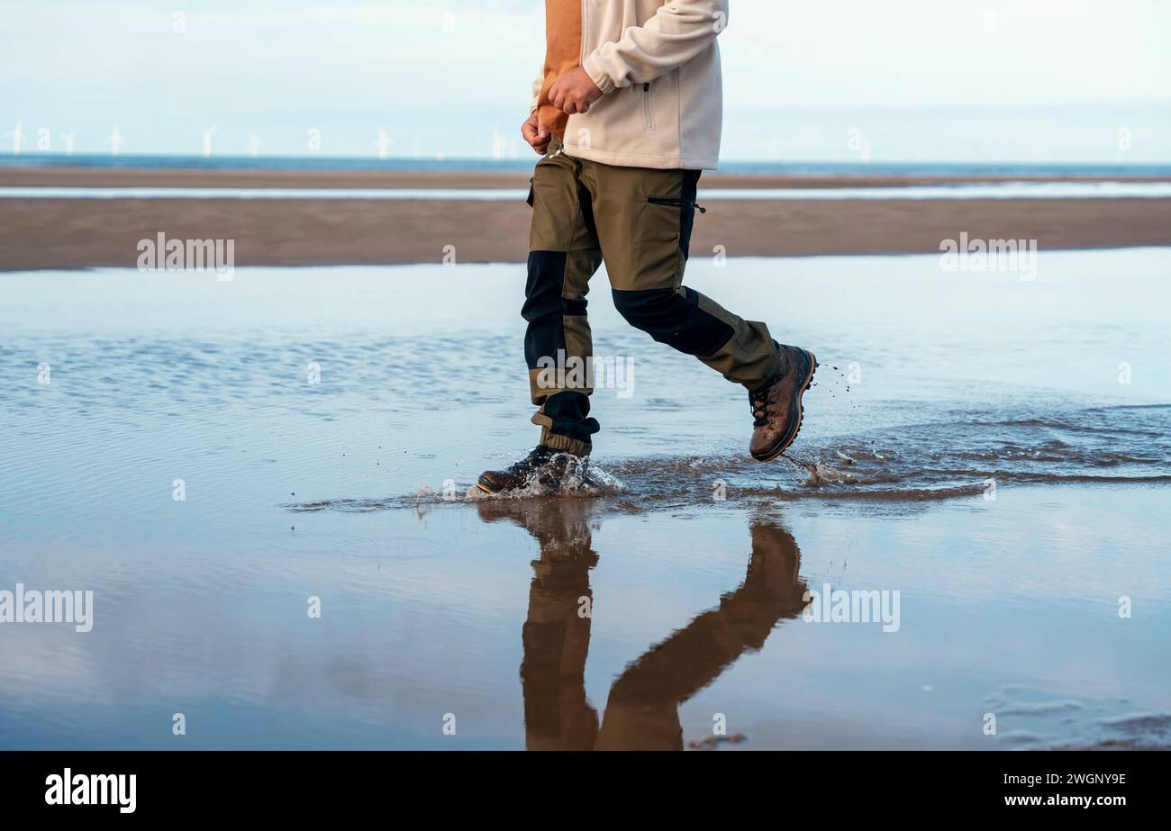 homme en pantalon waterproove et bottes courir sur la plage. Concept de style de vie de voyage Banque D'Images