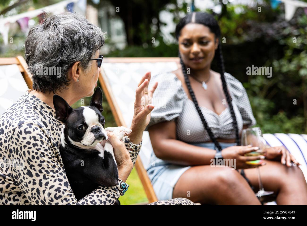La femme blanche mature avec un chien Boston terrier est profondément en conversation avec une jeune femme noire lors d'une fête dans le jardin en été Banque D'Images