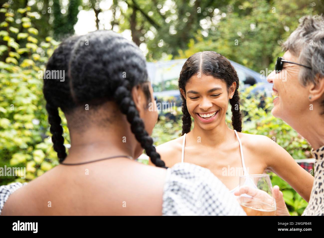 Une femme blanche mature discute et rit avec deux jeunes femmes noires lors d'une fête dans le jardin Banque D'Images