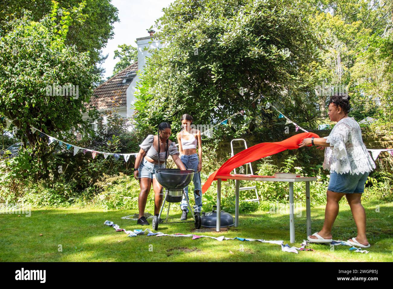 Une famille décorent le jardin avec une banderole et se préparent pour une fête barbecue Banque D'Images