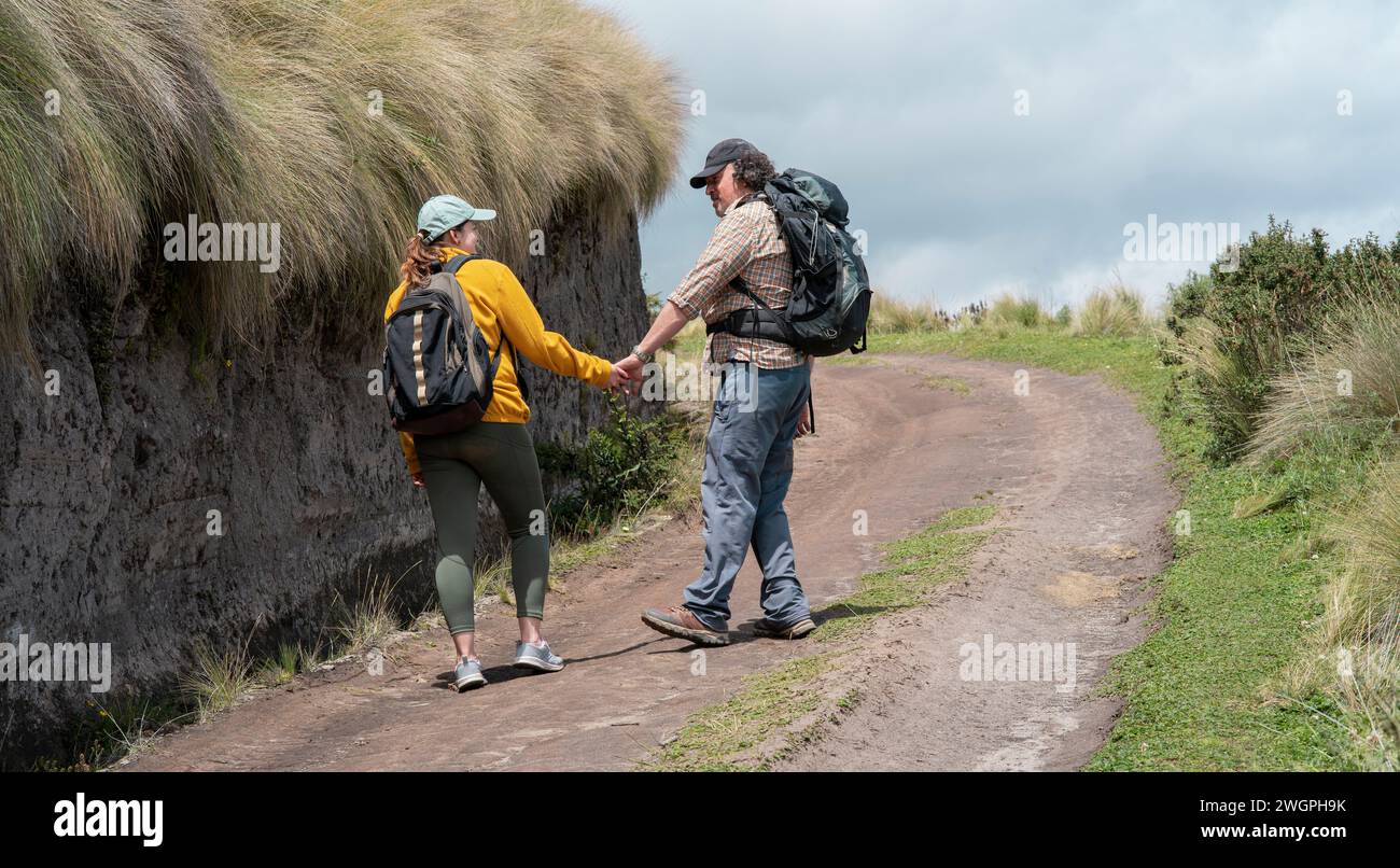 Jeune couple latino-américain avec des sacs à dos marchant la main sur un sentier au milieu de la friche sur une montagne pendant une journée ensoleillée Banque D'Images