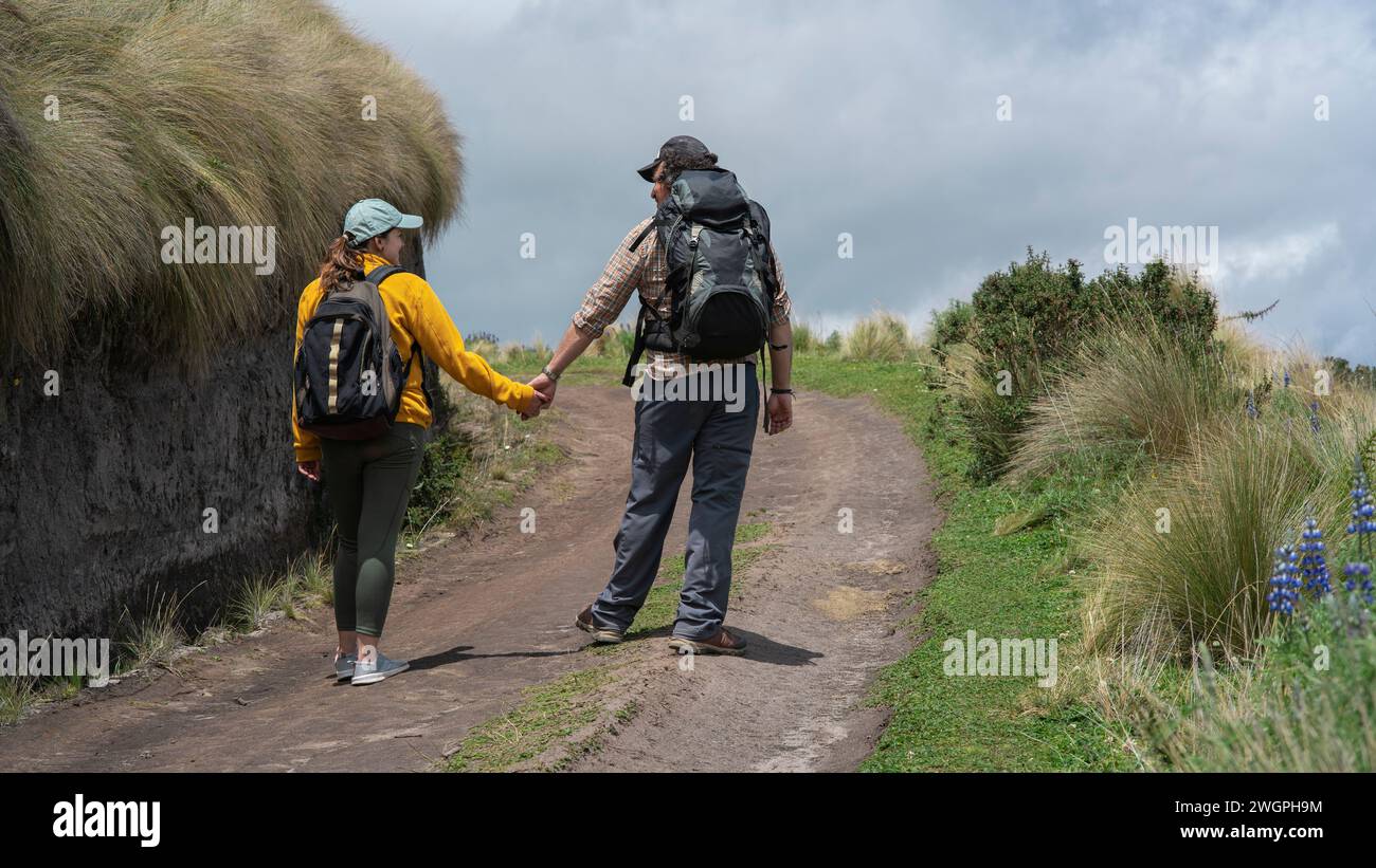 Jeune couple latino-américain avec des sacs à dos marchant la main sur un sentier au milieu de la friche sur une montagne pendant une journée ensoleillée Banque D'Images