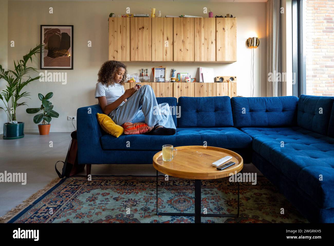 Fille adolescente de race mixte assise sur le canapé avec son téléphone relaxant Banque D'Images