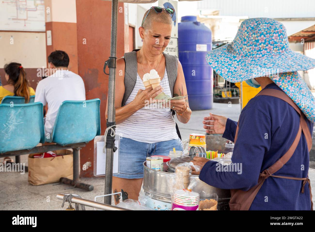 Femme d'âge moyen, Voyageur solo achète de la crème glacée à un vendeur de rue dans une station de bus dans le nord de la Thaïlande Banque D'Images