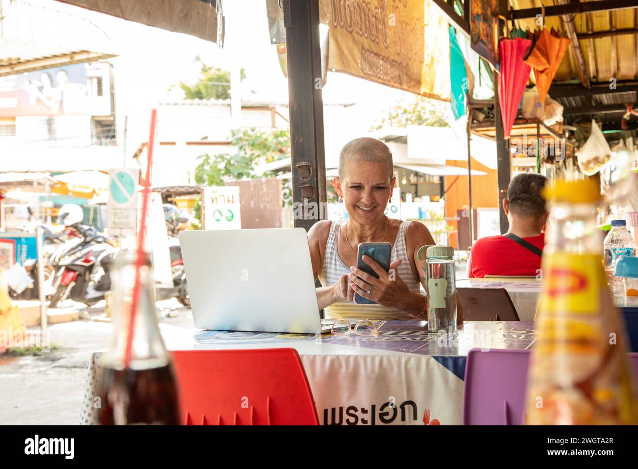 Femme mi-âgée voyelle solo est assise dans un restaurant local en utilisant son téléphone et son ordinateur portable Banque D'Images