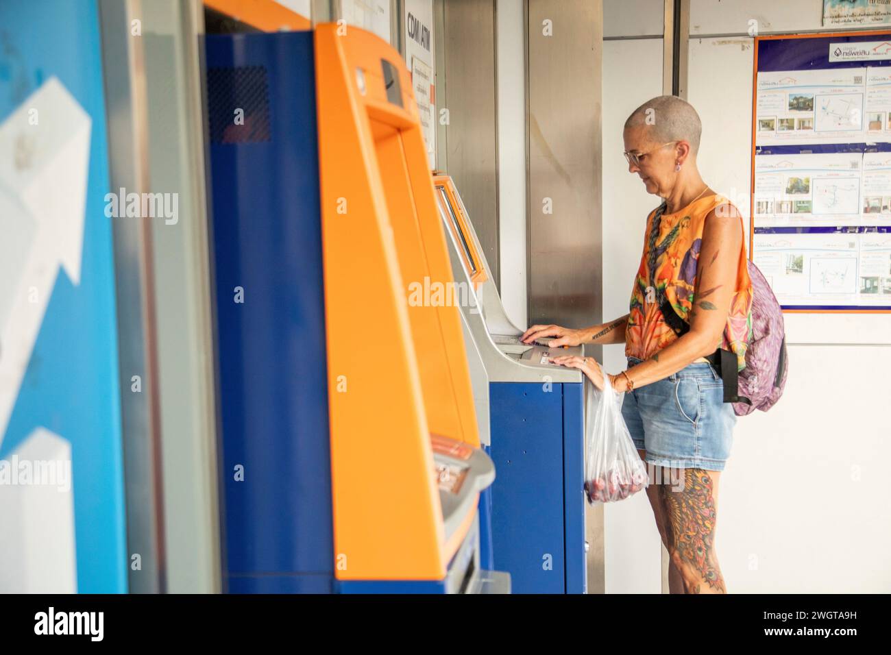 Femme mi-âgée voyageuse solo, s'arrête à l'ATM pour retirer la monnaie locale, elle a l'air sérieuse. Banque D'Images