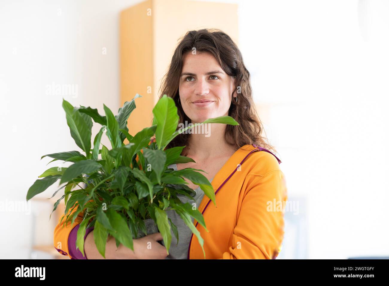 jeune femme avec veste jaune et plante verte à la maison Banque D'Images