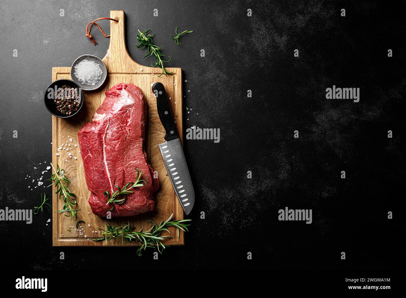 Entrecote de viande de boeuf sur une planche à découper, filet de viande de boeuf crue sur fond noir, vue de dessus Banque D'Images