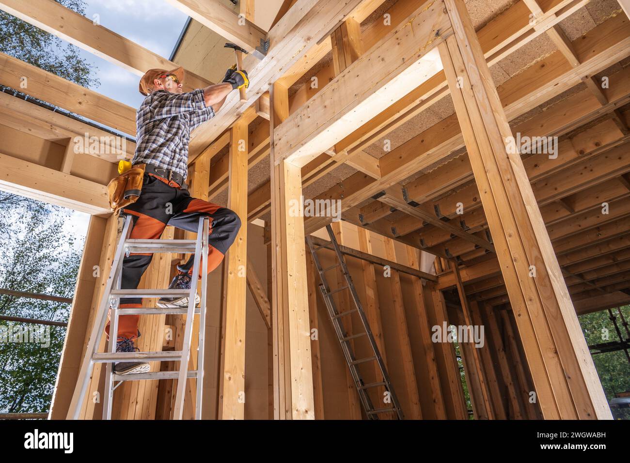 Bâtiment à ossature de bois de maison par un travailleur entrepreneur. Utilisation du marteau tout en restant sur une échelle Banque D'Images