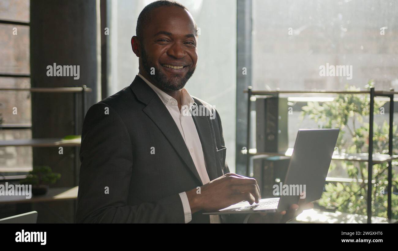 Mature homme d'affaires d'entrepreneur d'âge moyen homme d'affaires afro-américain dans le bureau ensoleillé d'entreprise travaillant avec le site Web de navigation de données numériques de recherche d'ordinateur portable Banque D'Images