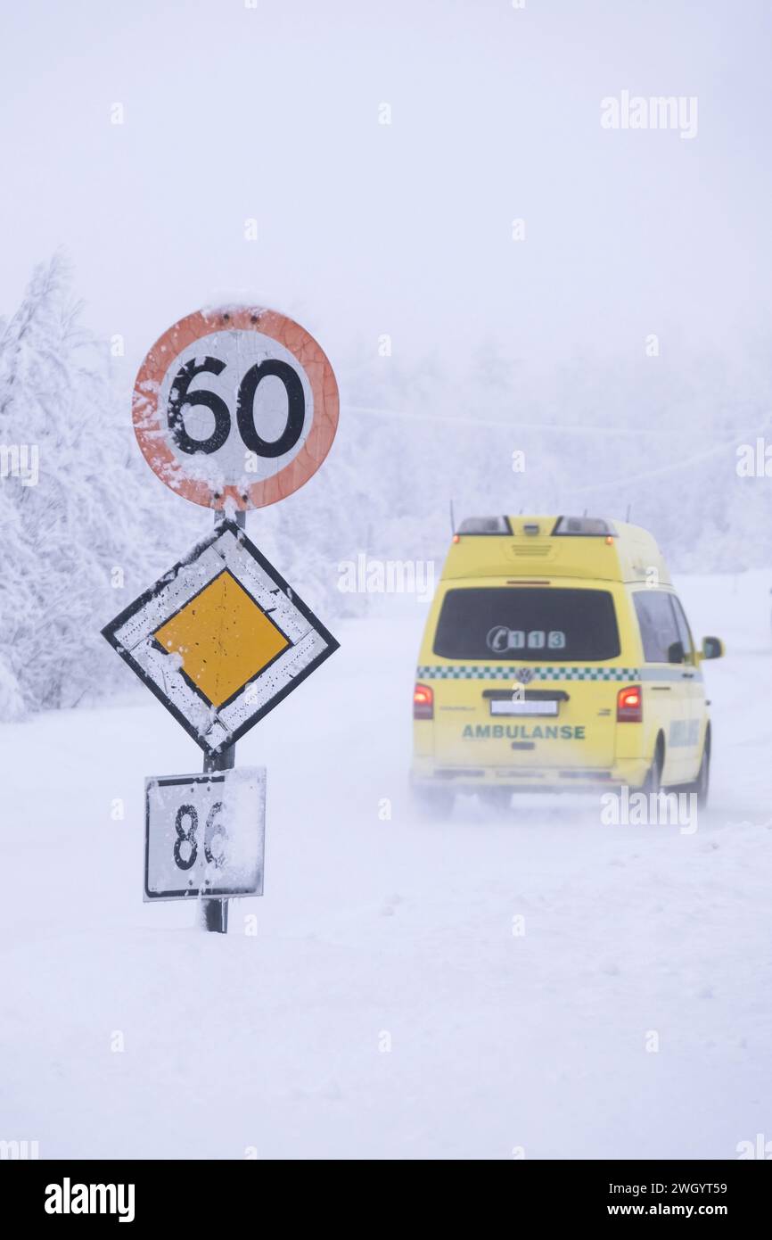 Ambulance passant une vitesse de 60 km/h et panneaux routiers prioritaires dans des conditions de conduite glacées sur une autoroute à Senja, Norvège, Scandinavie, Europe Banque D'Images