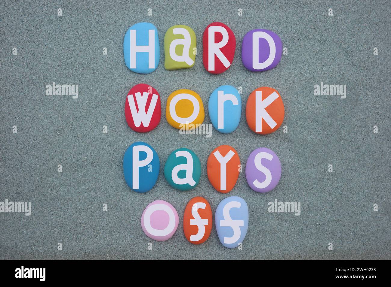 Hard Work rapporte, slogan motivant composé de lettres en pierre multicolores peintes à la main sur du sable vert Banque D'Images
