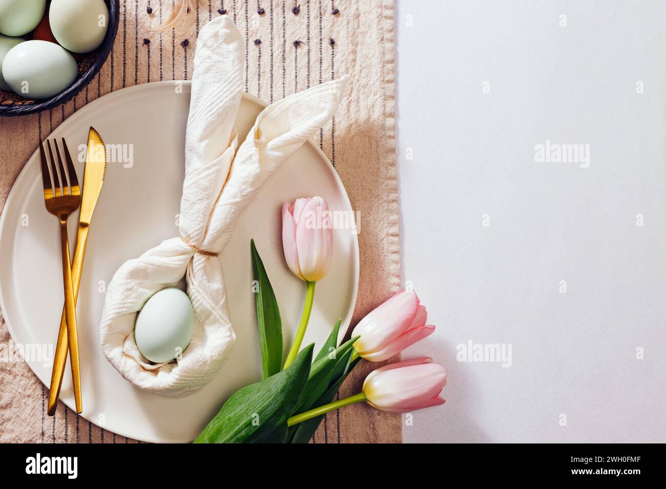 Table de Pâques, serviette pliée en forme de lapin , oeuf bleu et tulipes roses. Nature morte du printemps, vue de dessus Banque D'Images