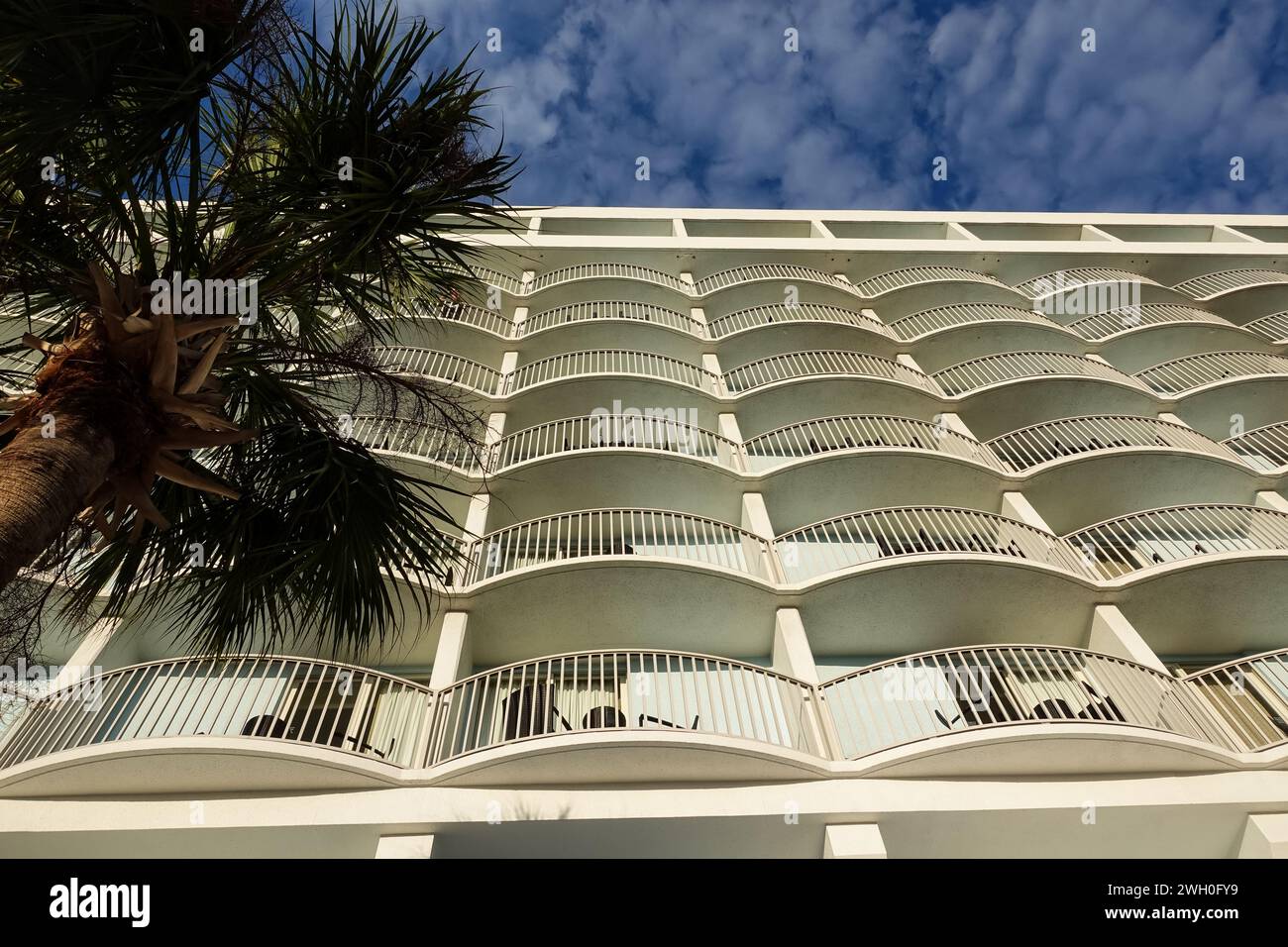 Hôtel blanc symétrique avec balcons, entouré de palmiers sous un ciel bleu ensoleillé Banque D'Images