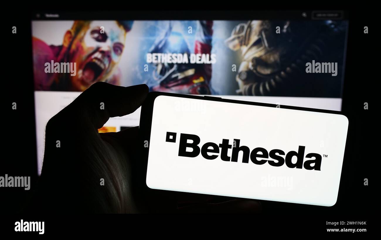 Personne tenant le téléphone portable avec le logo de la société américaine de jeux vidéo Bethesda Softworks LLC en face de la page Web. Concentrez-vous sur l'affichage du téléphone. Banque D'Images Personne tenant le téléphone portable avec le logo de la société américaine de jeux vidéo Bethesda Softworks LLC en face de la page Web. Concentrez-vous sur l'affichage du téléphone. Banque D'Images