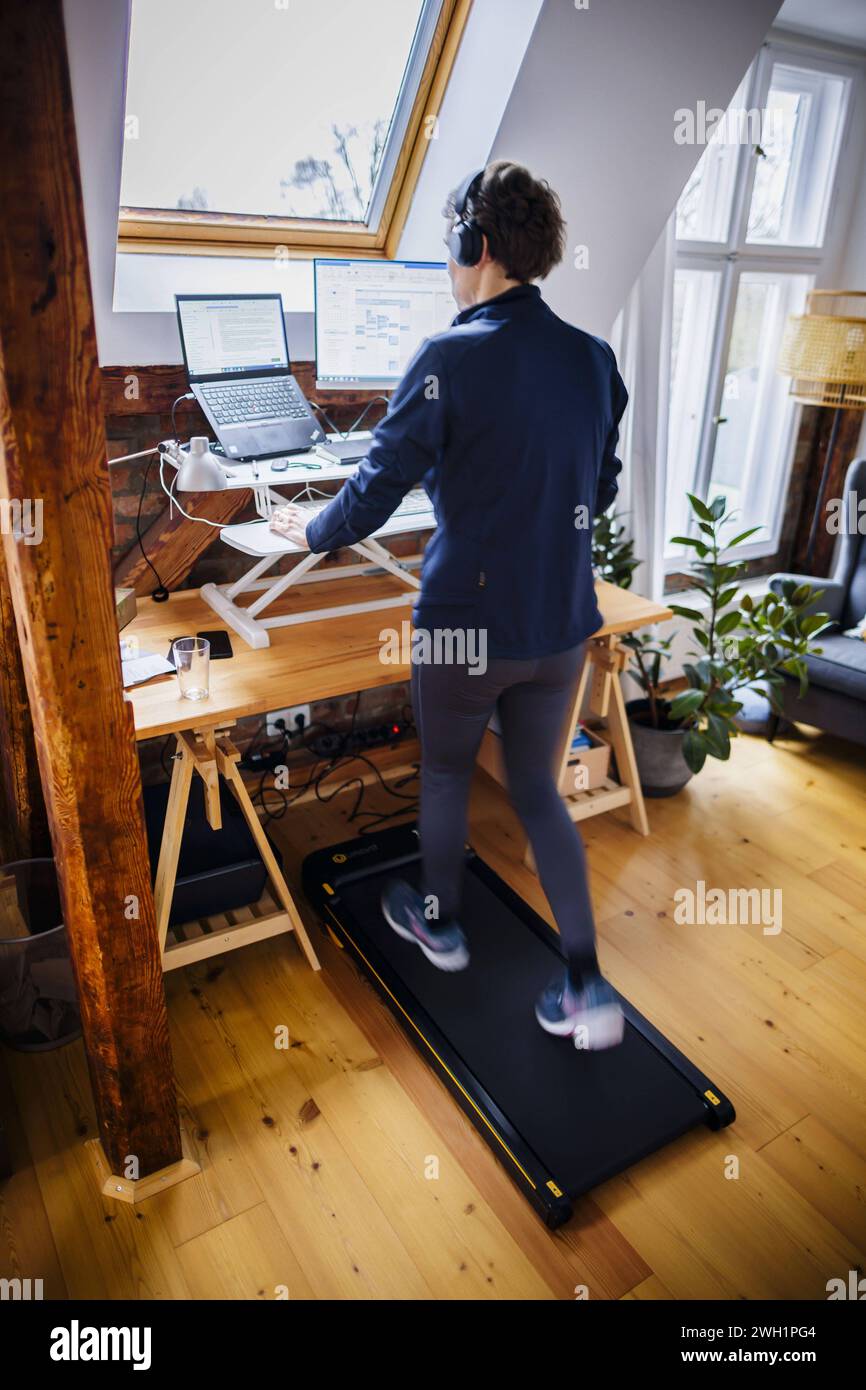 Eine Frau laeuft waehrend der Arbeit zu Hause im Home Office an ihrem Schreibtisch auf einem Walking Pad. Berlin, 07.02.2024. Berlin Deutschland *** A Banque D'Images
