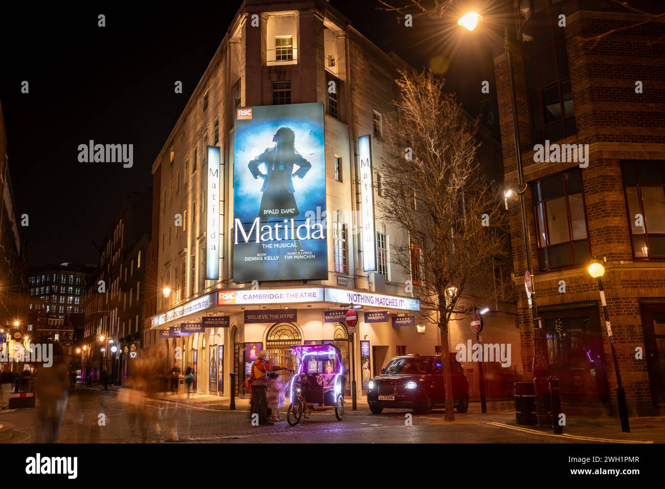 Londres. UK- 02.04.2024. Une vue extérieure nocturne du Cambridge Theatre montrant la façade, l'entrée et le panneau d'affichage de la comédie musicale Matilda. Banque D'Images