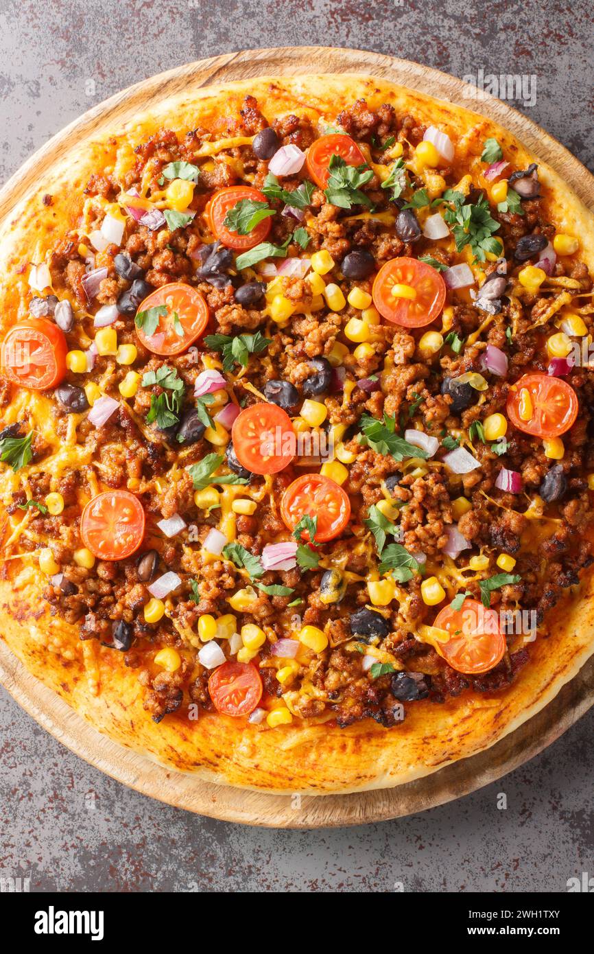 Pizza Tex Mex taco avec bœuf haché, tomates, maïs, haricots noirs, fromage cheddar, gros plan oignon rouge et épices mexicaines sur une planche de bois sur la table Banque D'Images