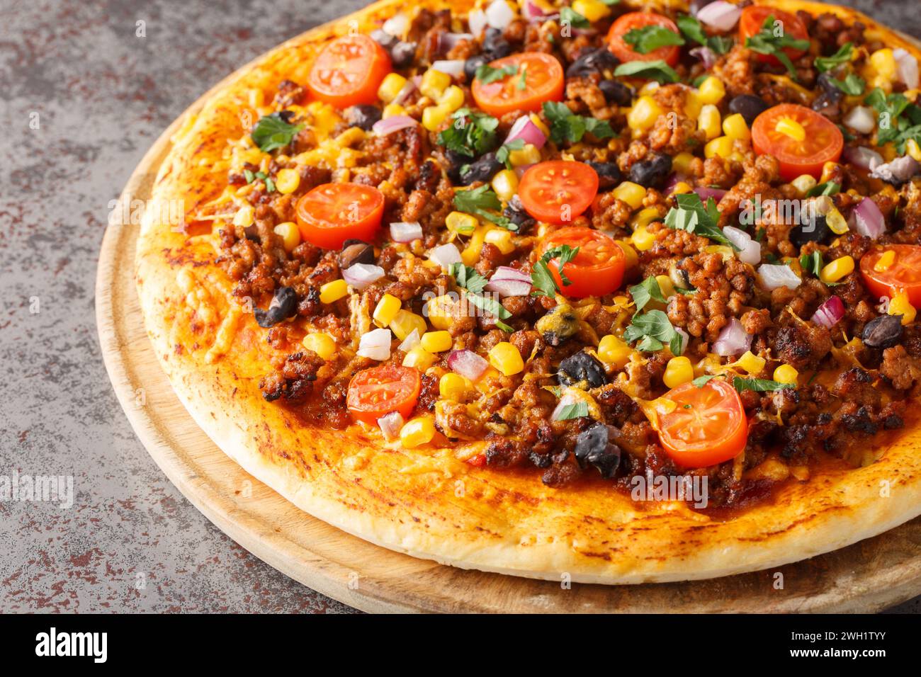 Pizza épicée mexicaine Taco avec bœuf haché, tomates, maïs, haricots noirs, fromage cheddar, oignon rouge sur la planche de bois sur la table. Horizontal Banque D'Images