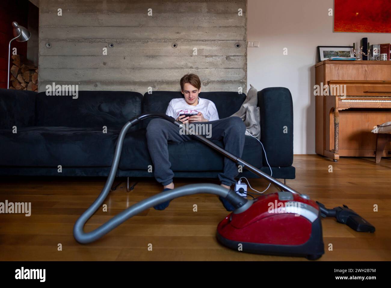 adolescent garçon assis sur l'entraîneur avec un téléphone intelligent au lieu de faire l'aspirateur Banque D'Images