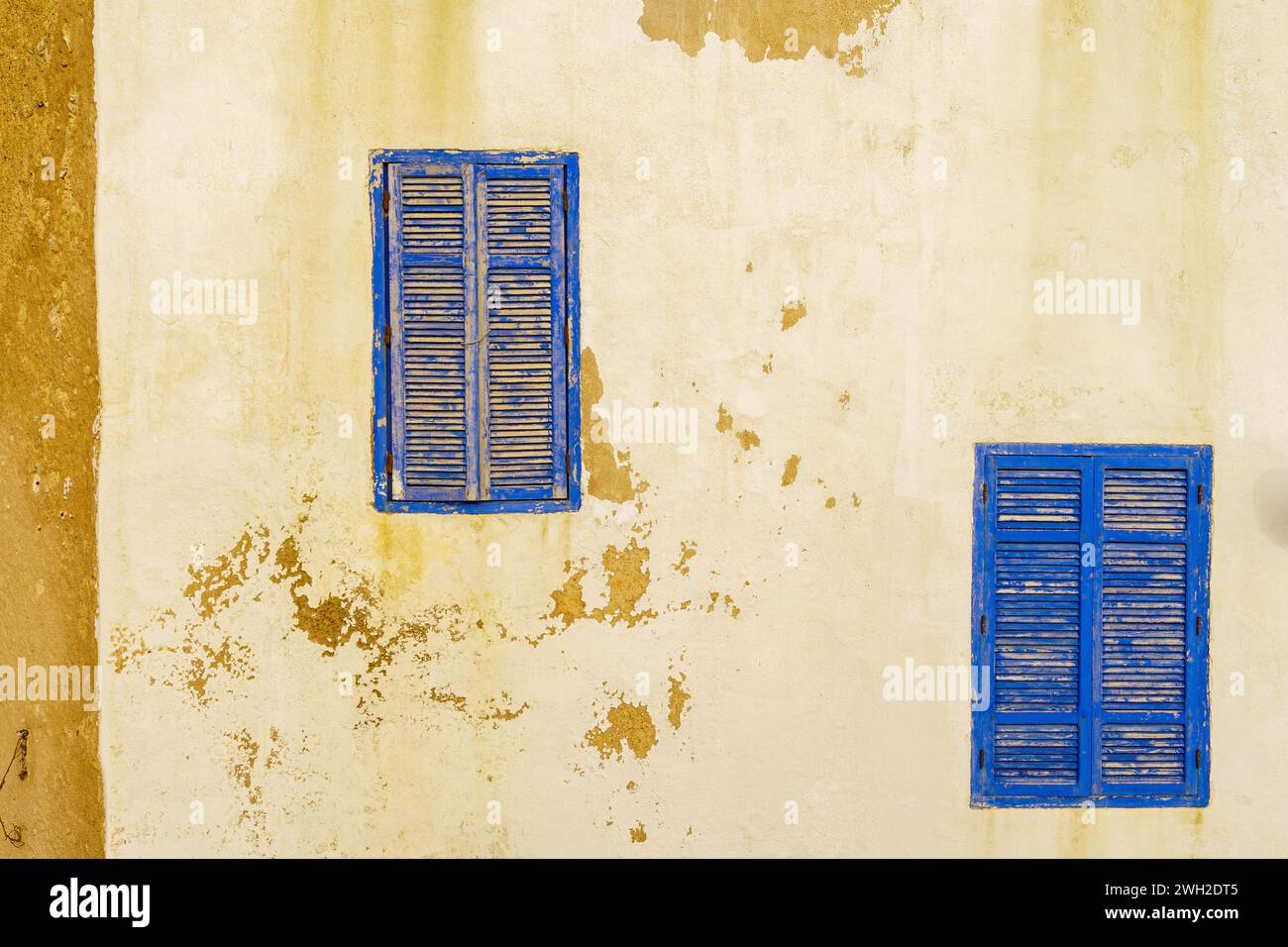 Vue sur les fenêtres bleues et les volets sur un mur de la vieille maison avec de la peinture blanche. Essaouira (Mogador), Maroc Banque D'Images