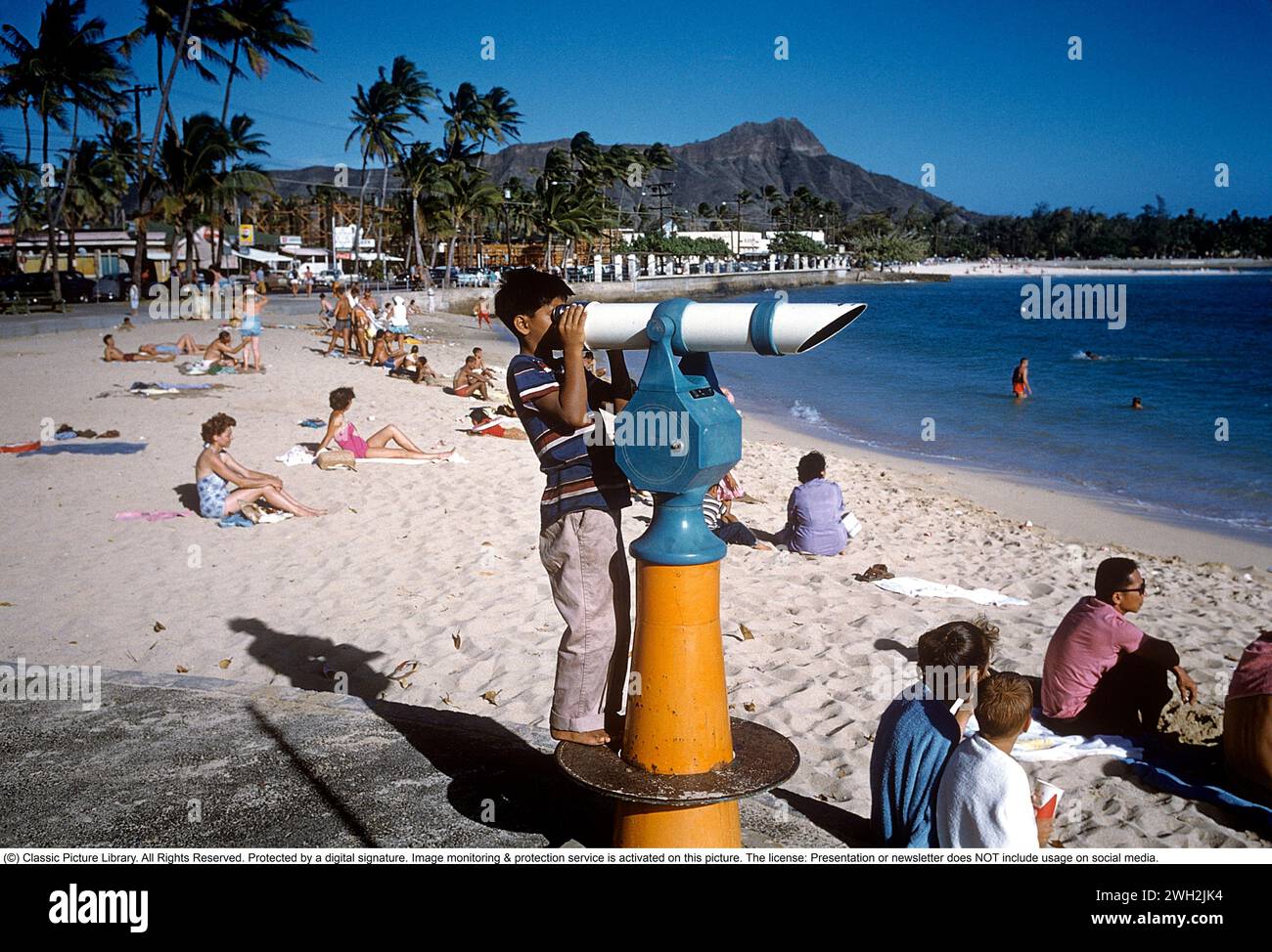 Honolulu Hawaï États-Unis. Une journée ensoleillée à la plage avec des gens dans le sable avec une vue sur le littoral et la montagne. 1959. Anders Svahn ref SVA9 Banque D'Images