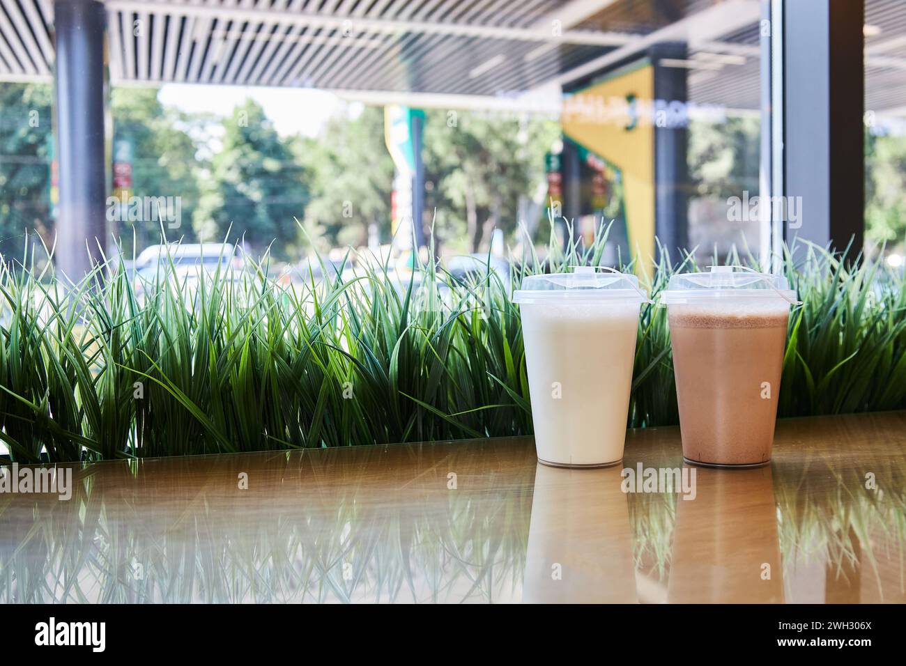 Milk-Shake à emporter, café-restaurant au magasin de la station-service. Deux gobelets en plastique transparent avec couvercles remplis de milk-shakes au chocolat et à la vanille sur la table, herbe verte. Bla Banque D'Images