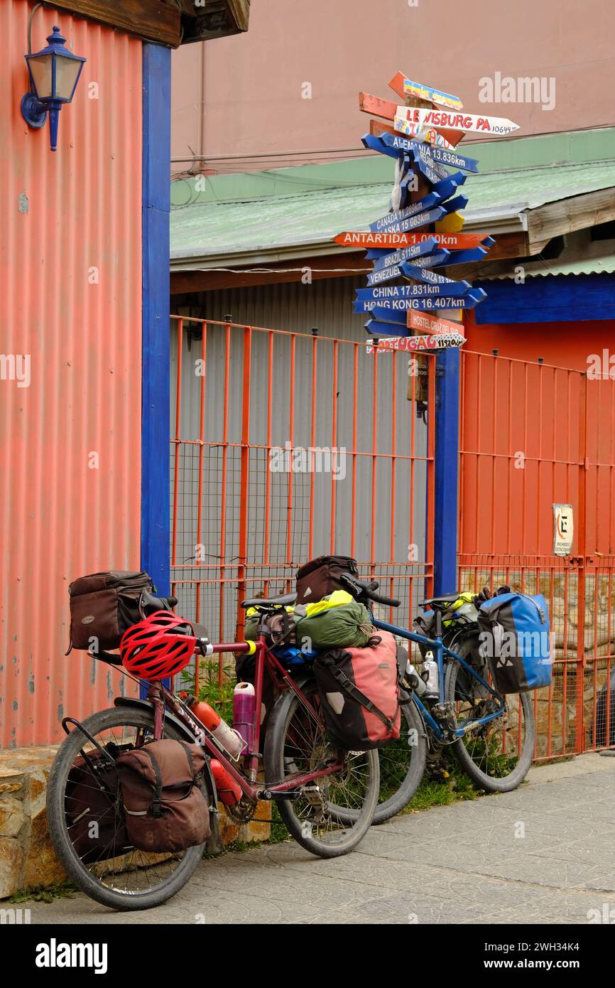 Deux vélos de tourisme chargés à côté d'un panneau indiquant un certain nombre de destinations mondiales à Ushuaia, en Argentine. Banque D'Images