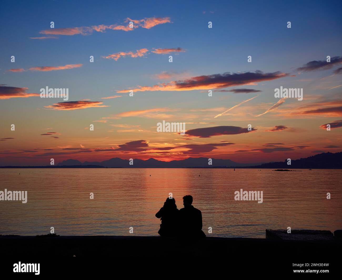 Coucher de soleil romantique sur la baie de Cannes, Riviera, France avec un jeune couple assis et silhouetté contre la mer rose. Banque D'Images