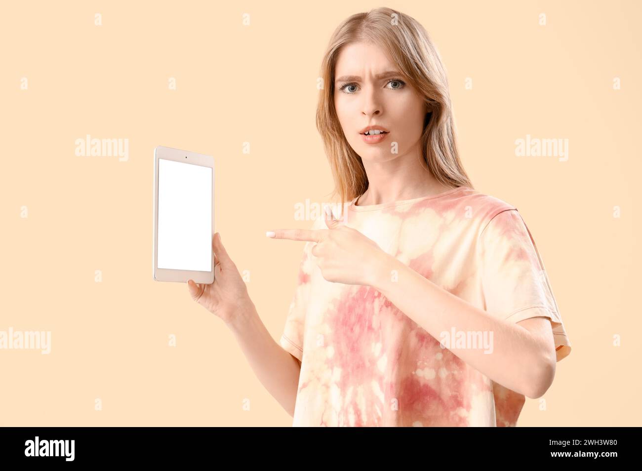 Jeune femme pointant vers l'ordinateur tablette sur fond beige. Concept d'accusation Banque D'Images