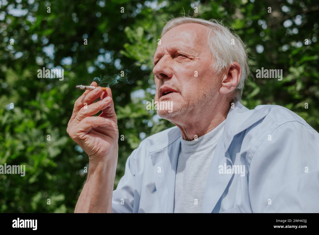 Vieil homme fumant une cigarette dans une journée d'été ensoleillée, tir franc adapté aux discussions sur le mode de vie et le vieillissement, malsain Banque D'Images