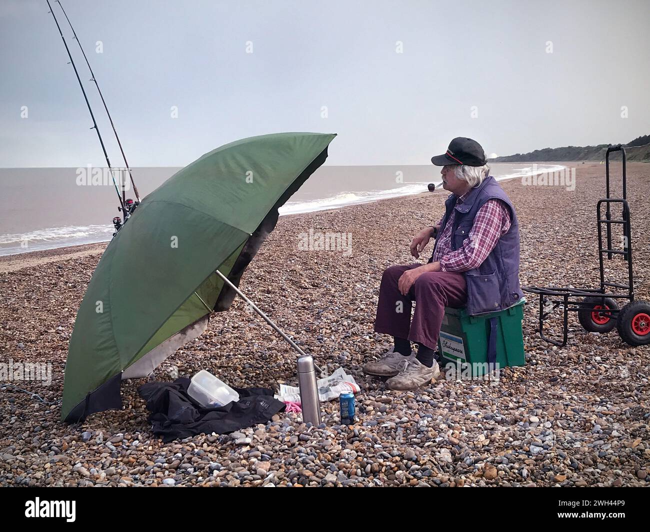 homme plus âgé fumant pipe pêche sur la plage à dunwich suffolk angleterre Banque D'Images