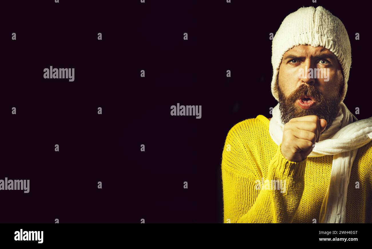 L'homme tousse. Homme malade toussant dans son poing. Homme beau barbu en pull, chapeau et foulard toussant. Homme souffrant de grippe ou de pneumonie. Homme malade avec Banque D'Images