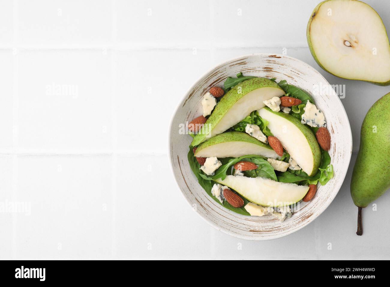 Délicieuse salade de poires dans un bol et fruits sur une table carrelée légère, vue de dessus. Espace pour le texte Banque D'Images